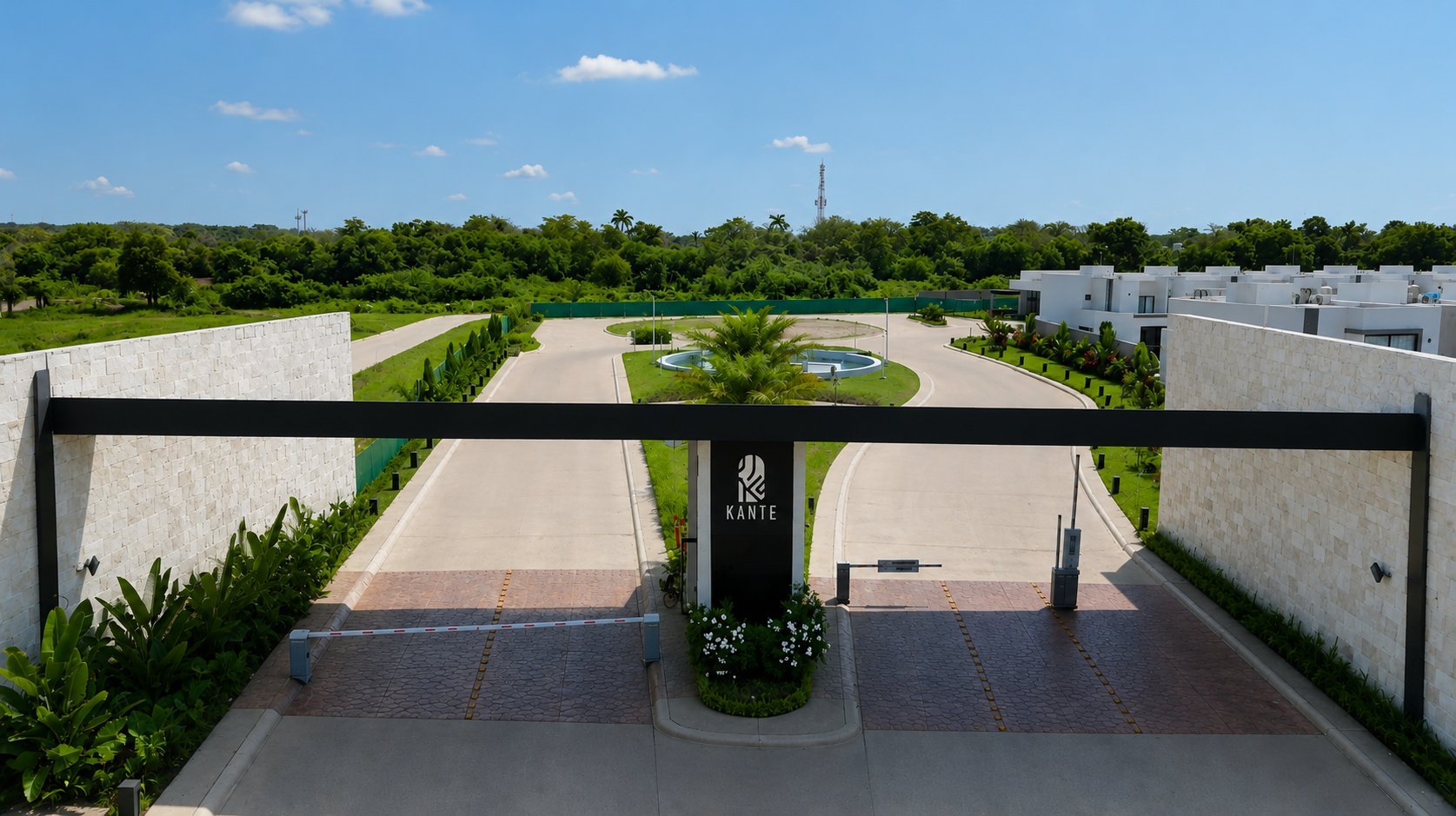 Aerial view of gated modern residential community with manicured landscape and tree-lined entrance under blue sky