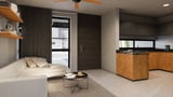 Modern studio apartment with cream sofa, wooden kitchen island, ceiling fan, and large windows overlooking city street