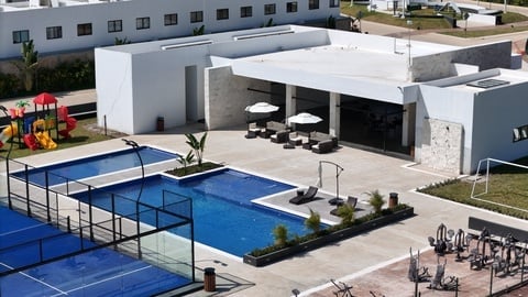 Aerial view of a modern sports facility with blue paddle tennis courts, a white building with covered seating area, and surrounding grounds