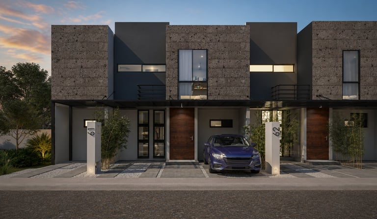 Modern duplex townhouses with brick and black panels, ground-level garages, parked cars, and landscaping at dusk