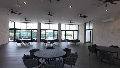 Modern spacious indoor venue with round dining tables, black chairs, large windows with views, ceiling fans, and polished flooring